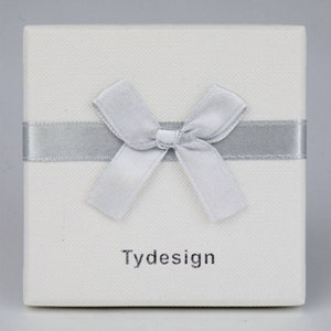 May include: A white gift box with a silver ribbon and bow. The box has the word "Tydesign" printed on the front.