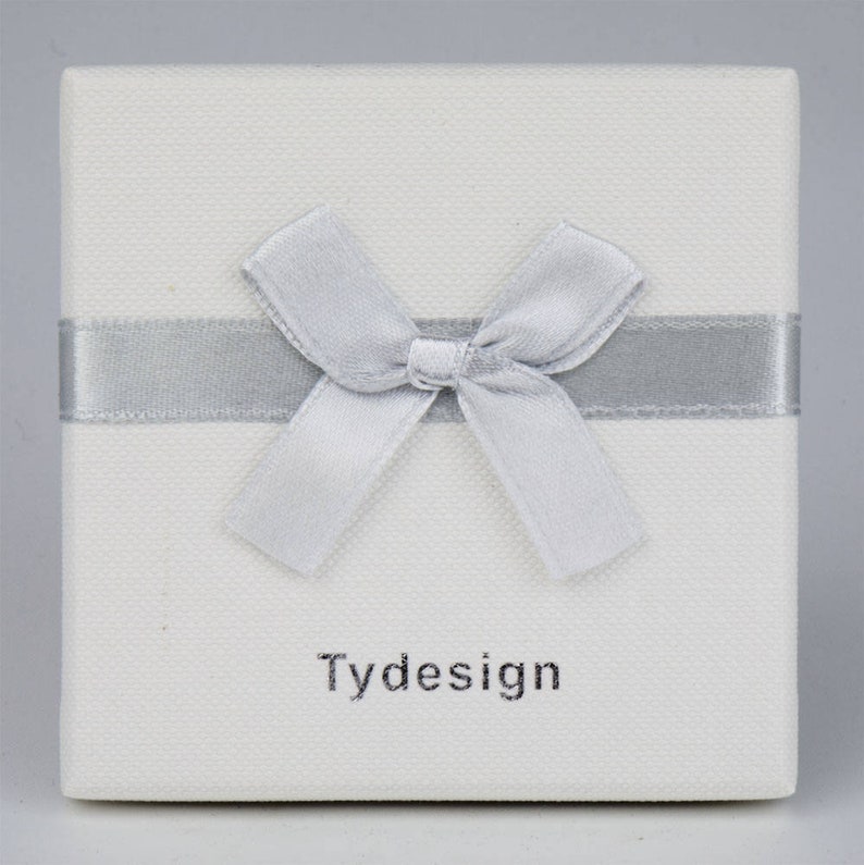 May include: A white gift box with a silver ribbon and bow. The box has the word "Tydesign" printed on the front.