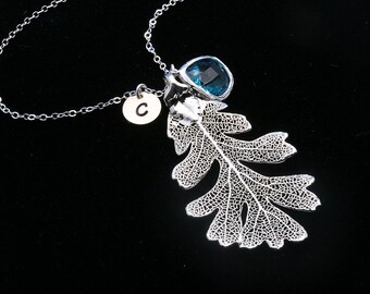 Puede incluir: Un collar de plata con un delicado colgante de hoja de roble, una piedra preciosa azul y un dije de plata con la letra 'C'.