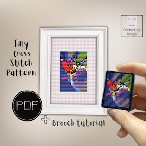 Puede incluir: Un marco blanco que contiene un patrón de punto de cruz de una figura con alas rojas y ropa azul sobre un fondo morado. El texto dice Tiny Cross Stitch Pattern, PDF, Brooch tutorial y Stitched Joy Design.