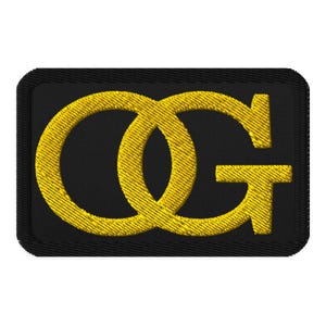 May include: A rectangular embroidered patch featuring a black background with a thick black border. The letters O and G are stitched in bright yellow thread, with the two letters overlapping in the center to form a singular graphic design.