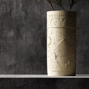 May include: A cylindrical beige vase with a wood-grain texture featuring an embossed relief of Egyptian pyramids, palm trees, and the sun. The text reads "EGYPT" at the top, "LAND OF PHARAOHS" at the bottom, and "EST. 1977" with Japanese characters.