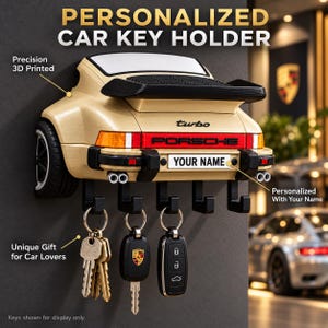 May include: A beige 3D printed wall-mounted car key holder shaped like the rear of a sports car. It features a black spoiler, the text turbo and PORSCHE, and a number plate area with the text YOUR NAME. Five black hooks hold three sets of keys.