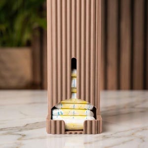 Peut inclure: Un distributeur rectangulaire vertical de couleur brun clair, doté d'une surface cannelée et d'une fente centrale révélant une pile de tampons emballés individuellement en blanc et jaune. L'objet présente une base plate et un design texturé.
