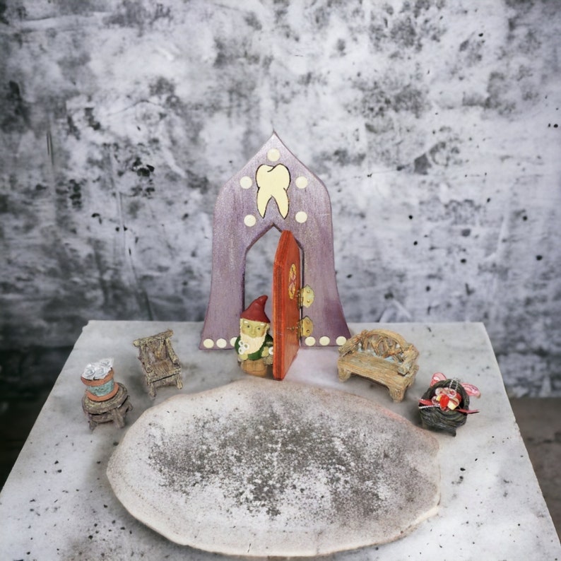 May include: A miniature wooden fairy house with a purple door and a tooth design. The house is surrounded by miniature furniture, including a chair, a bench, and a gnome figurine.