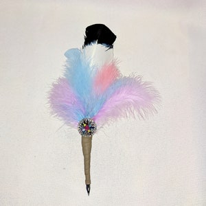 May include: A feather pen with a black and white feather, adorned with a colorful rhinestone embellishment and a brown wrapped handle.
