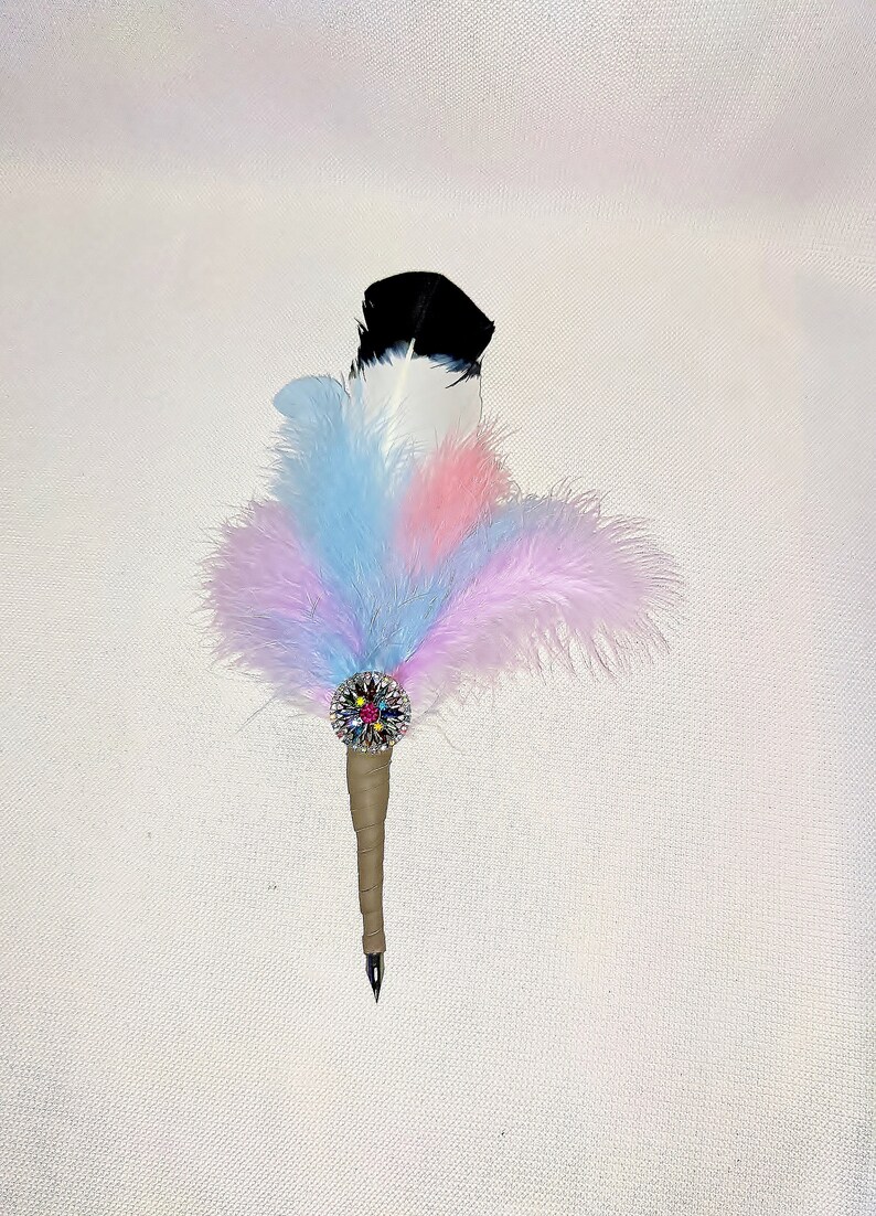 May include: A feather pen with a black and white feather, adorned with a colorful rhinestone embellishment and a brown wrapped handle.