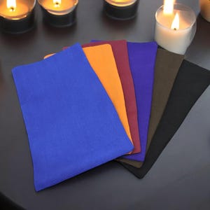 May include: Six fabric swatches in different colors, including blue, orange, red, purple, green, and black, are arranged in a fan shape on a dark surface.
