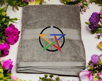 May include: A gray towel with a colorful embroidered pentagram in the center. The pentagram is surrounded by a black circle. The towel is surrounded by flowers.