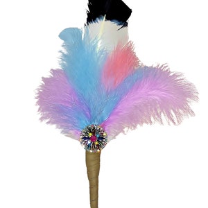 May include: A colorful feather pen with a jeweled embellishment. The pen has a black, white, pink, and blue feather plume. The pen is made of wood and has a metal nib.