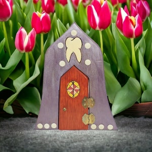 May include: A purple wooden fairy house with a red door and a tooth design. The house is surrounded by pink tulips.