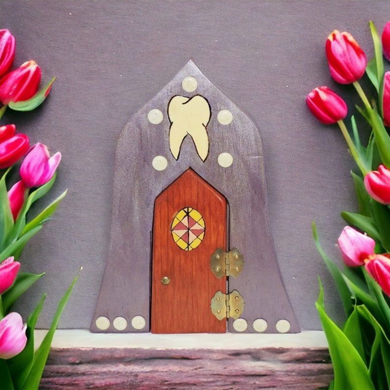 May include: A purple wooden fairy door with a tooth design and a small red wooden door with a stained glass window. The door is surrounded by pink tulips.