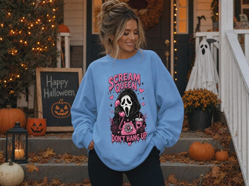 May include: A light blue crewneck sweatshirt featuring a graphic print of a masked figure in a black hooded robe holding a pink rotary telephone. The text reads "SCREAM QUEEN" and "DON'T HANG UP" in pink, surrounded by pink hearts and roses.