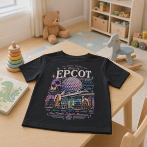 May include: A black short-sleeve t-shirt featuring a graphic print of the Epcot Spaceship Earth structure, a monorail, and various international pavilion landmarks with the text "this is EPCOT", "Different by Design", and "One World, Infinite Memories".