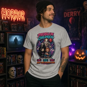 Puede incluir: Una camiseta gris claro de manga corta con un estampado gr&aacute;fico de tres personajes de pel&iacute;culas de terror. El texto dice "PROBLEM CHILDREN" y "MOST LIKELY TO CAUSE A SCENE", junto con etiquetas para "CLASS CLOWN", "BIGGEST CALLER" y "SHORTEST TEMPER".