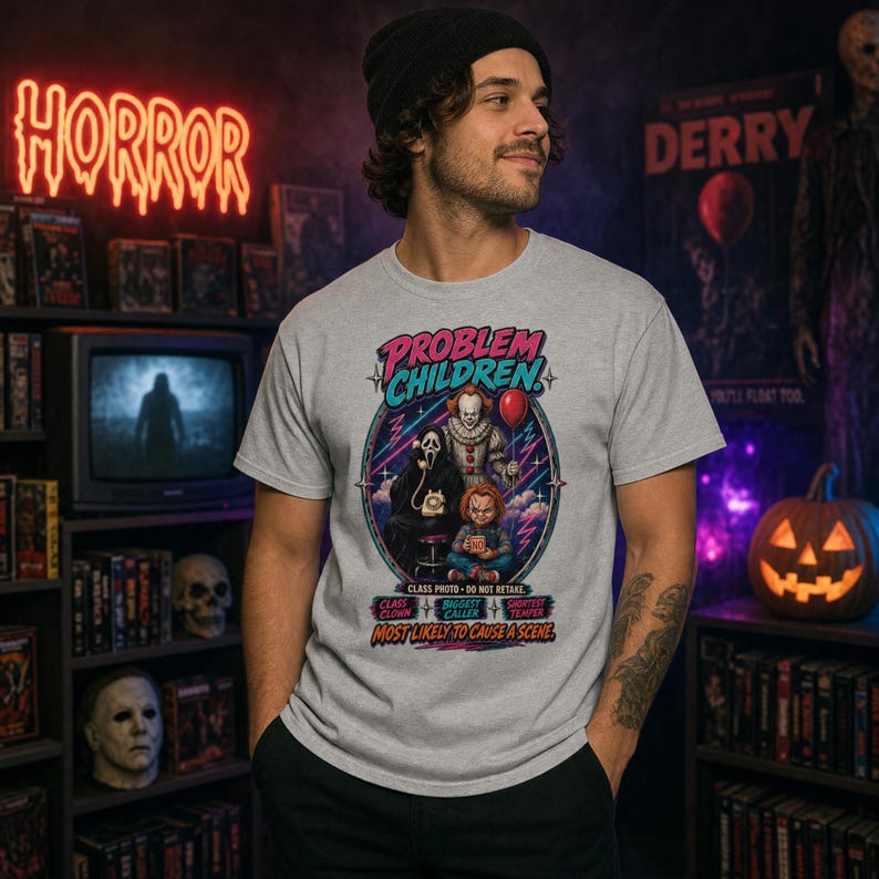 Puede incluir: Una camiseta gris claro de manga corta con un estampado gr&aacute;fico de tres personajes de pel&iacute;culas de terror. El texto dice "PROBLEM CHILDREN" y "MOST LIKELY TO CAUSE A SCENE", junto con etiquetas para "CLASS CLOWN", "BIGGEST CALLER" y "SHORTEST TEMPER".