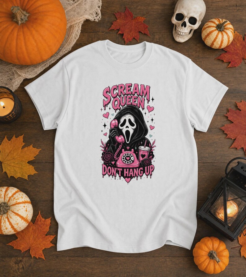 May include: A white t-shirt featuring a graphic of a hooded figure with a white mask holding a pink rotary telephone. The text reads "SCREAM QUEEN" and "DON'T HANG UP" in pink, with pink hearts, stars, and a pink drink cup surrounding the figure.