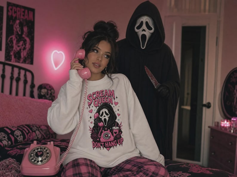 May include: A white long-sleeve sweatshirt featuring a graphic print of a masked figure holding a pink rotary phone, surrounded by pink hearts and stars. The text reads "SCREAM QUEEN" at the top and "DON'T HANG UP" at the bottom in pink lettering.