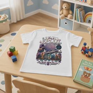 May include: A white short-sleeve t-shirt featuring a colourful graphic print of Epcot. The design includes the Spaceship Earth geosphere, a monorail, and various international pavilion landmarks with the text This is EPCOT and One World, Infinite Memories.