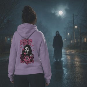 May include: A light purple hooded sweatshirt featuring a graphic on the back. The design includes a masked figure holding a pink telephone, a pink rotary phone, and a drink cup, with the text "SCREAM QUEEN" and "DON'T HANG UP" in pink.