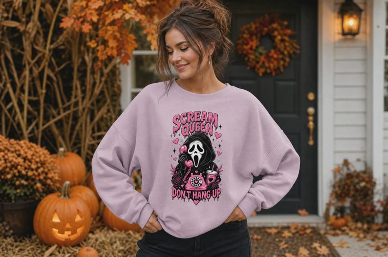 May include: A light purple crewneck sweatshirt featuring a graphic print of a hooded figure in a mask holding a pink rotary telephone. The text reads SCREAM QUEEN and DON'T HANG UP in pink lettering, surrounded by small hearts and star accents.