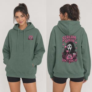 May include: A sage green hooded sweatshirt featuring a small pink rotary phone graphic on the front left chest. The back displays a large graphic of a masked figure holding a pink rotary phone with the text Scream Queen Don't Hang Up.
