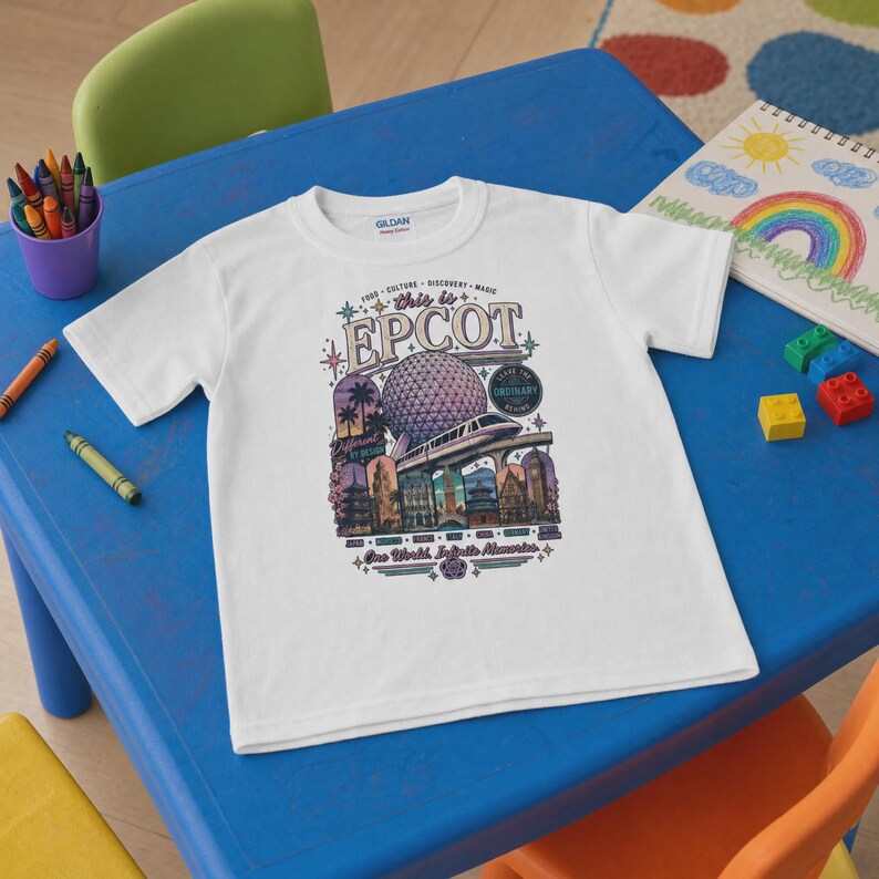 May include: A white short-sleeve t-shirt featuring a colourful graphic print that says "this is EPCOT" with illustrations of the Spaceship Earth geosphere, a monorail, and various international pavilion landmarks, surrounded by stars and text.