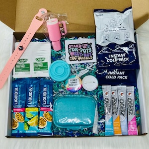 May include: A gift box containing a pink silicone wristband, two Curad alcohol prep pads, a pink tumbler keychain, a blue lid, a sticker reading STAND UP FOR POTS BUT NOT TOO QUICKLY, two instant cold packs, a button, and electrolyte drink packets.
