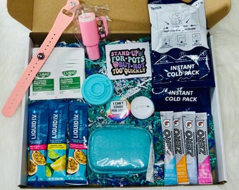 Op de afbeelding: Een geschenkdoos met een roze siliconen polsbandje, twee Curad alcoholdoekjes, een roze beker-sleutelhanger, een blauw deksel, een sticker met de tekst STAND UP FOR POTS BUT NOT TOO QUICKLY, twee instant coldpacks, een button en elektrolyt-drankzakjes.