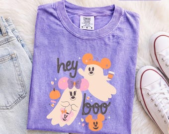 Könnte beinhalten: Ein violettes kurzärmeliges T-Shirt mit einer Grafik von zwei Geistern mit Mausohren, einem Kürbis und dem Text "hey boo". Das T-Shirt hat einen Rundhalsausschnitt und ein Comfort Colors Markenetikett an der Innenseite des Kragens.