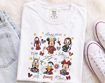 Könnte beinhalten: Ein weißes T-Shirt mit einem Grafikdruck verschiedener Zeichentrickfiguren, die als Superhelden verkleidet sind. Das Design zeigt Mickey Mouse, Goofy, Donald Duck, Daisy Duck, Minnie Mouse und Pluto sowie Avengers-Logos, Sterne und Charakter-Signaturen.