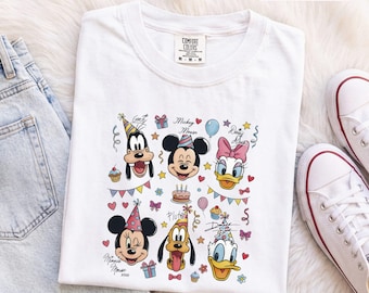 Könnte beinhalten: Ein weißes T-Shirt mit einem bunten Grafikdruck von Disney-Figuren, darunter Mickey Maus, Minnie Maus, Goofy, Pluto, Donald Duck und Daisy Duck mit Partyhüten, umgeben von Illustrationen von Kuchen, Luftballons und Geschenken.