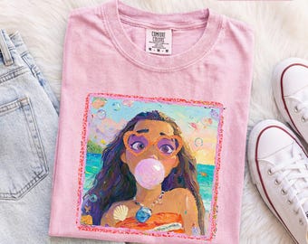 Könnte beinhalten: Ein hellrosa T-Shirt mit kurzen Ärmeln und einem quadratischen Grafikdruck einer Person mit langem dunklem Haar, die herzförmige Brillen trägt und eine rosa Kaugummiblase macht. Die Grafik zeigt eine Strandszene, eine Muschel und eine Halskette.