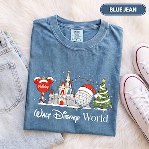 May include: A blue jean colored t-shirt featuring a graphic of a holiday-themed castle, a geodesic sphere wearing a Santa hat, and a Christmas tree, with the text Walt Disney World printed below in white script and sans-serif lettering.