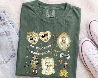Könnte beinhalten: Ein moosgrünes T-Shirt mit einem Grafikdruck von Disney-Figuren in Safari-Kleidung. Das Design zeigt Mickey und Minnie Mouse in herzförmigen Rahmen, Donald Duck, Goofy und Pluto sowie den Schriftzug "ANIMAL KINGDOM" auf einem Banner.