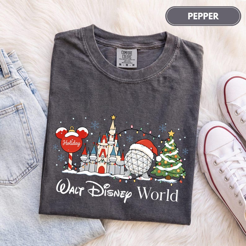 May include: A charcoal gray t-shirt featuring a graphic of a castle, a geodesic dome wearing a Santa hat, a Christmas tree, and a Mickey Mouse-shaped ornament. The text reads Walt Disney World. The shirt has a crew neck and short sleeves.