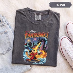 May include: A charcoal gray t-shirt featuring a graphic of Mickey Mouse as a sorcerer casting a spell with water and fire. The design includes a large dragon, fireworks, and the text Disney's Fantasmic! in a stylized yellow and purple font.