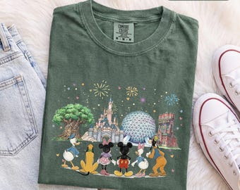 Könnte beinhalten: Ein moosgrünes Kurzarm-T-Shirt mit einer Grafik von Disney-Figuren, darunter Donald Duck, Pluto, Minnie Maus, Mickey Maus, Daisy Duck und Goofy, die vor einem Schloss und einer geodätischen Kuppel mit Feuerwerk stehen.