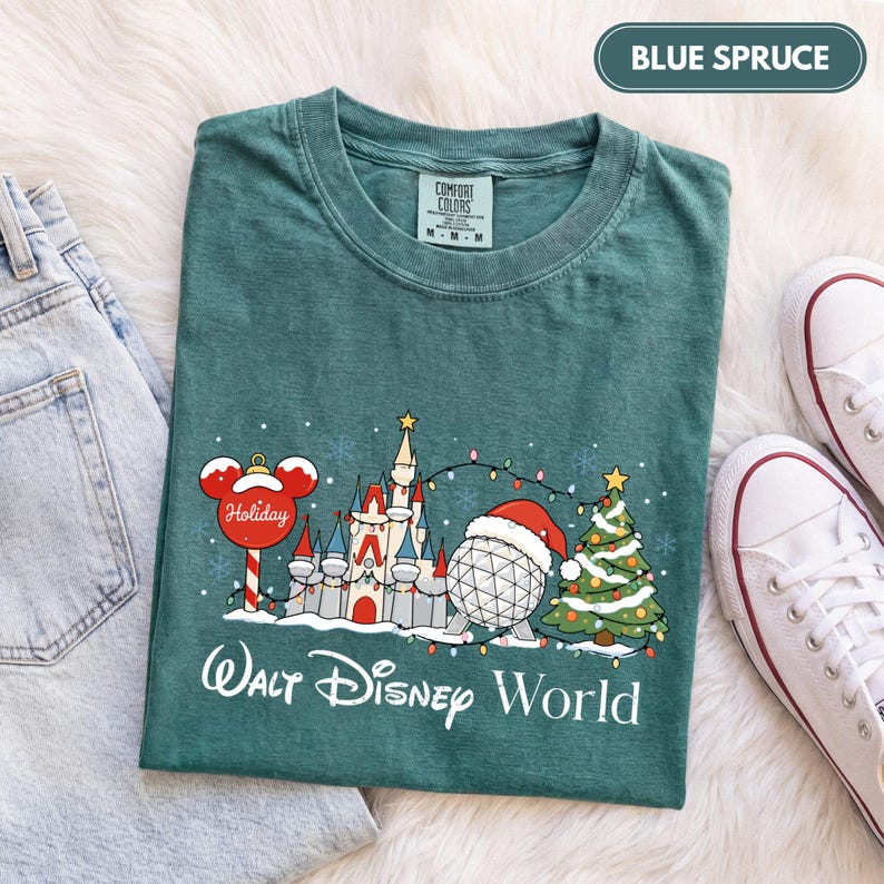May include: A blue spruce colored t-shirt featuring a graphic of a castle, a geodesic sphere wearing a Santa hat, a Christmas tree, and a Mickey Mouse ornament. The text Walt Disney World is printed below the graphic in white script lettering.