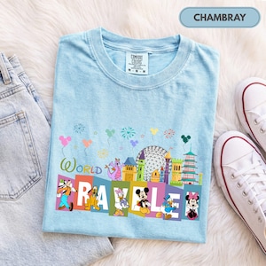 May include: A light blue crew neck t-shirt featuring a graphic print with the text "WORLD TRAVELER" and various Disney characters including Mickey Mouse, Minnie Mouse, Donald Duck, Daisy Duck, Pluto, Goofy, and Figment, along with park landmarks.