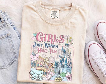 Könnte beinhalten: Ein elfenbeinfarbenes T-Shirt mit einem Grafikdruck, der den Text "GIRLS JUST WANNA HAVE FUN" über einem Schloss, einer Teetasse, einem Popcorn-Eimer, einem Getränk und einer Fee zeigt. Das Design enthält Feuerwerk und Mausohr-Symbole.