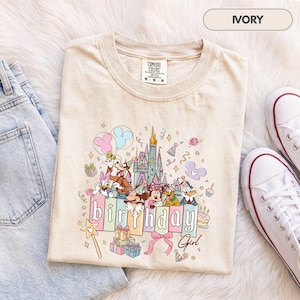 Könnte beinhalten: Ein elfenbeinfarbenes T-Shirt mit einem Grafikdruck von einem Schloss, Mickey Maus, Minnie Maus, Donald Duck, Daisy Duck, Goofy und Pluto. Der Text "birthday" ist in großen Blockbuchstaben gedruckt, "Girl" steht darunter in Schreibschrift.