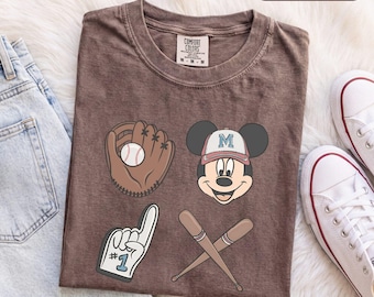 Könnte beinhalten: Ein espressofarbenes T-Shirt mit einem Grafikdruck, der einen Baseballhandschuh mit Ball, eine Zeichentrickmaus mit einer Baseballkappe mit dem Buchstaben M, einen Schaumstofffinger mit der Nummer 1 und zwei gekreuzte Baseballschläger zeigt.