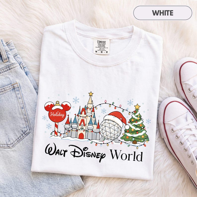 May include: A white short-sleeve t-shirt featuring a graphic of a castle, a geodesic dome wearing a Santa hat, a Christmas tree, and a Mickey Mouse ornament. The text Walt Disney World is printed below the graphic in a black script font.