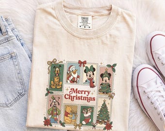 Könnte beinhalten: Ein elfenbeinfarbenes T-Shirt mit einem Grafikdruck von Disney-Figuren in rechteckigen Rahmen und dem Text Merry Christmas. Das Design zeigt Pluto, Donald Duck, Minnie Maus, Micky Maus, Goofy, Winnie Puuh sowie Chip und Chap.