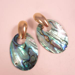 May include: A pair of oval earrings featuring iridescent abalone shells and gold-coloured metal details. The earrings have a gold-coloured post and a loop connecting to the abalone shell. The shells display blue, green, and purple tones.