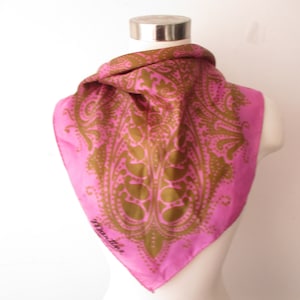 Peut inclure: Un foulard en soie rose avec un motif cachemire dans les tons or et marron. Le foulard est de forme carrée et porte le mot "Martine" en écriture cursive dans le coin inférieur droit.