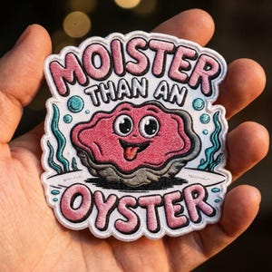 May include: A white embroidered patch featuring a pink cartoon oyster with a face and tongue sticking out. The text reads MOISTER THAN AN OYSTER in pink letters with black outlines. The design includes teal seaweed and blue bubbles on a white background.