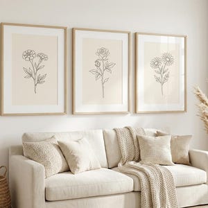 May include: A set of three framed wall art prints featuring black line drawings of flowers on a light beige background. Each print is encased in a light wood frame, displaying a different botanical illustration of a flower with leaves.