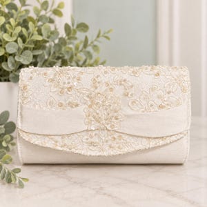 May include: An ivory clutch bag featuring an intricate floral lace overlay adorned with small clear beads and sequins. A horizontal satin band crosses the front flap, which is finished with a scalloped edge and a central beaded floral motif.